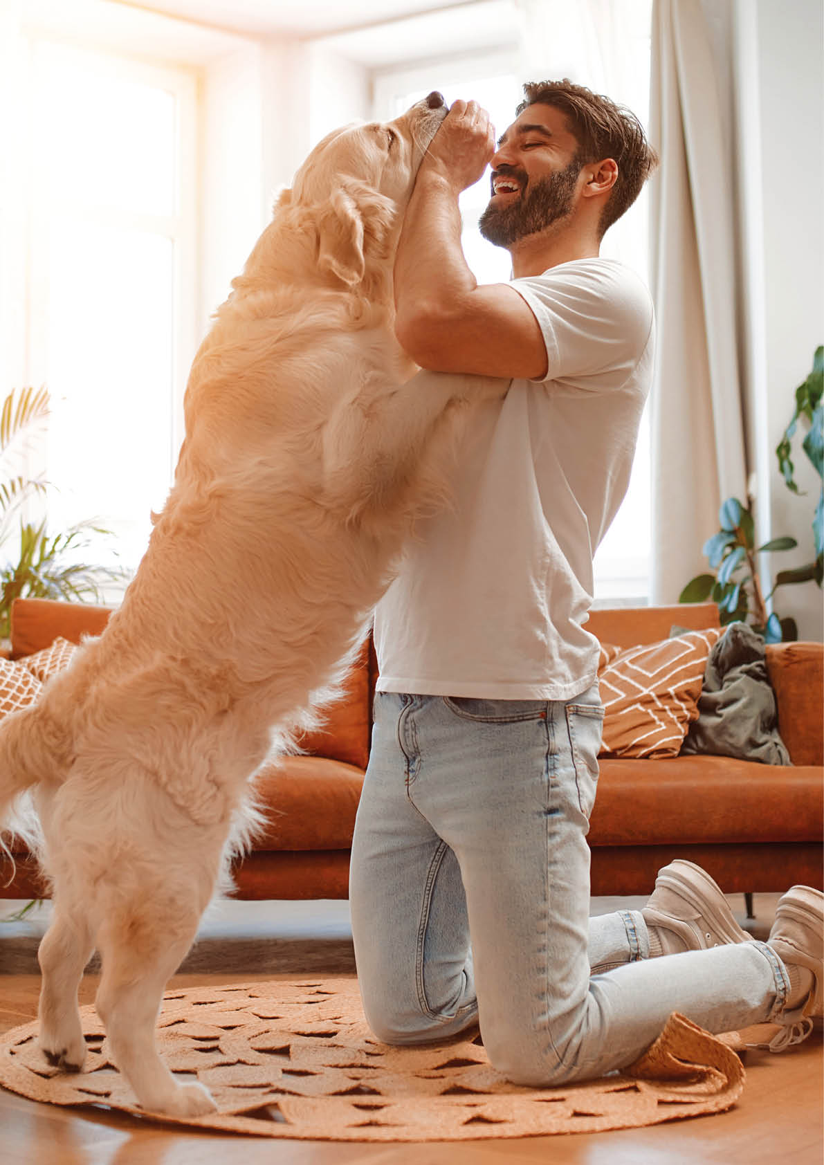 Handsome bearded man playing and training his labrador dog while sitting on the floor in the living room at home, having fun together.