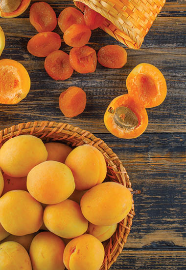 Apricots with dried apricots in a wicker basket on wooden background, top view. 