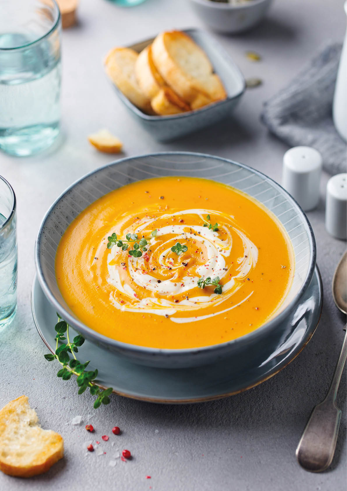 Pumpkin and carrot soup with cream on grey stone background.