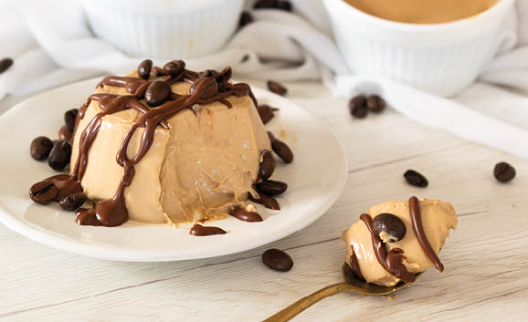 Traditional Italian dessert, coffee Panna Cotta, on a white plate, garnished with melted chocolate and chocolate chips.